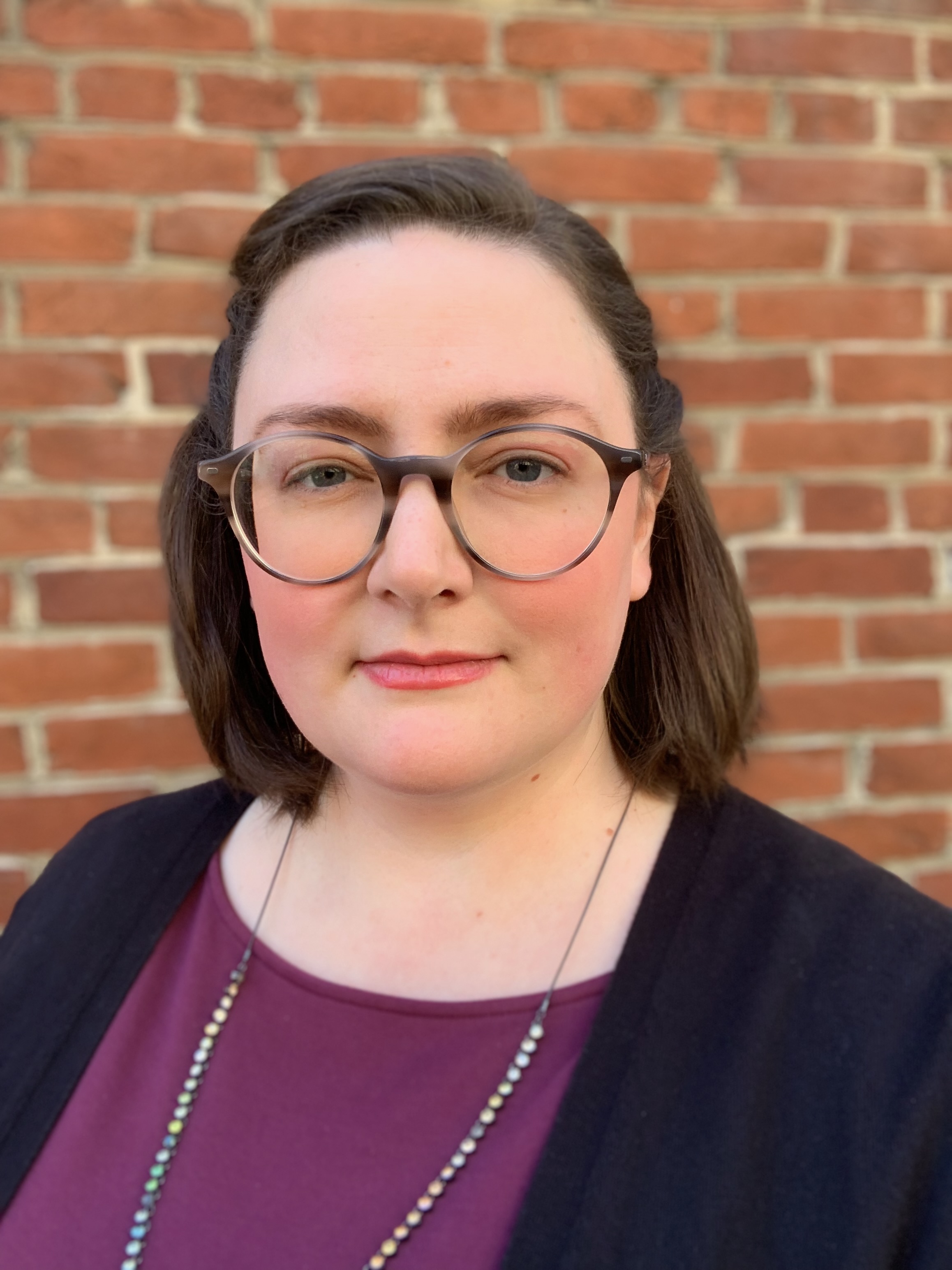 Portrait of Dr. Emily Snuff. She's wearing a purple shirt, dark blue cardigan in front of a brick wall.